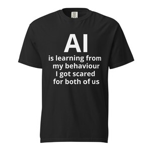 May include: Black t-shirt with white text. The text reads "AI is learning from my behaviour I got scared for both of us". The shirt has a crew neck and short sleeves. The shirt is made of a soft material.