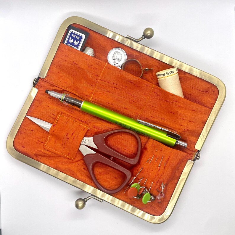 May include: An orange fabric sewing kit with a brass clasp. The kit contains a pencil, scissors, thread, needles, and a thimble.