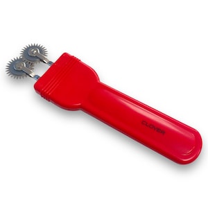 May include: Red plastic handled double-sided rotary cutter with two metal wheels. The handle has the word "CLOVER" printed on it.