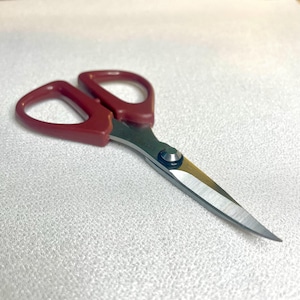 May include: Red handled scissors with a silver blade. The scissors have a small silver knob in the center of the handles.