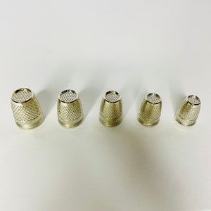 以下が含まれることがあります： 大小の異なる銀製の指ぬきが5つ、大きい順に並んでいます