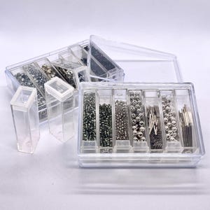 May include: Clear plastic bead storage containers filled with various sizes and colors of beads. The containers are rectangular with individual compartments, and some have lids. The beads include silver, black, and iridescent colors, perfect for jewelry making.