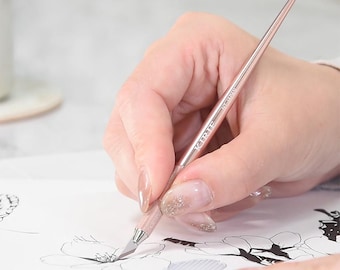 May include: A rose gold craft knife with a sharp blade is held over a black and white floral drawing. The knife has the text "KIRTE" on the handle. The image shows the knife in use, suggesting precision and detail work.