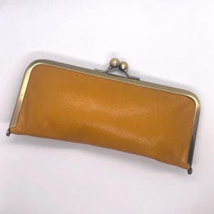 May include: A mustard yellow leather wallet with a brass clasp and two round knobs.