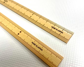 Puede incluir: Dos reglas de madera con marcas negras y el texto "MADE IN JAPAN" impreso en ellas.