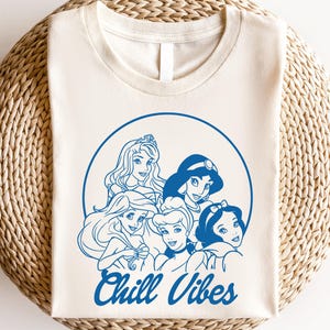 Minimalist blue line art of Disney princesses with "Chill Vibes" text on cream t-shirt; features Ariel, Cinderella, Snow White, Belle, and Jasmine in a relaxed, modern design.
