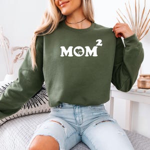 May include: A green sweatshirt with the text "MOM²" in white with a heart symbol in the middle of the "O".