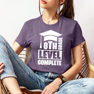 May include: Purple t-shirt with white text that reads "8th Grade Level Complete" with a graduation cap graphic.