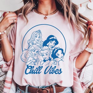 Minimalist blue line art of Disney princesses with "Chill Vibes" text on cream t-shirt; features Ariel, Cinderella, Snow White, Belle, and Jasmine in a relaxed, modern design.