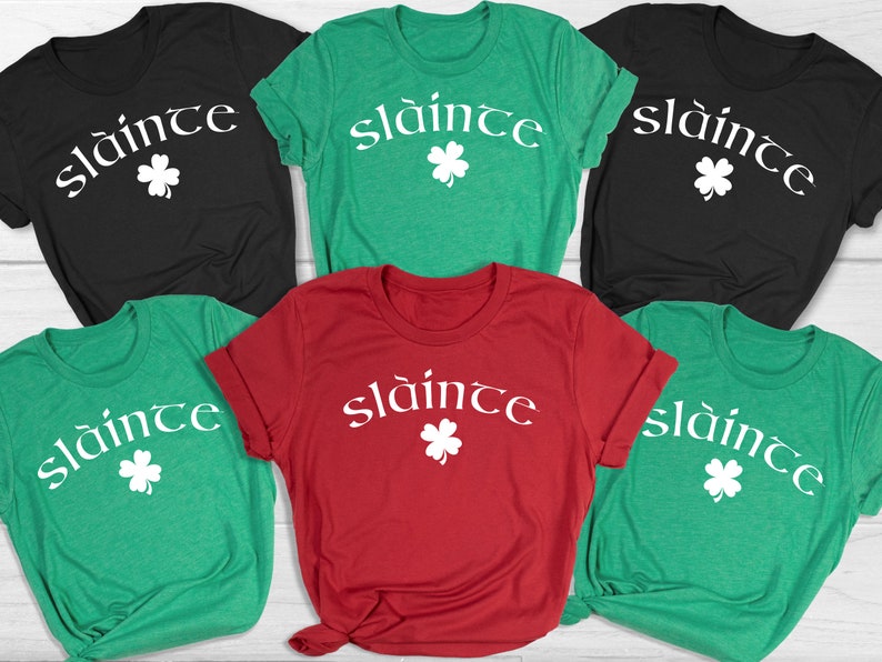 Op de afbeelding: Vijf T-shirts in verschillende kleuren met de Ierse zin "sl&aacute;inte" en een klavertje vier bedrukt op de voorkant.
