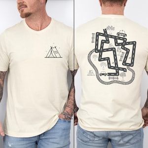 May include: A cream colored t-shirt with a black outline of a tent on the front and a black and white illustration of a road with trees, cars, and a train track on the back.