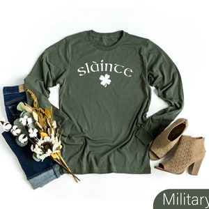 Op de afbeelding: Een longsleeve t-shirt in militaire groene kleur met het woord "sl&aacute;inte" in witte letters en een wit klavertje vier.