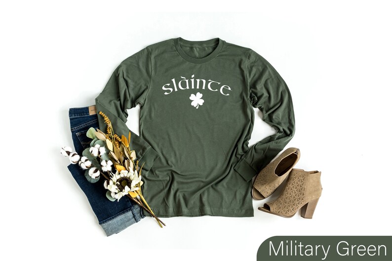 Op de afbeelding: Een longsleeve t-shirt in militaire groene kleur met het woord "sl&aacute;inte" in witte letters en een wit klavertje vier.