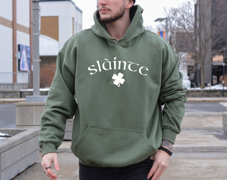 Op de afbeelding: Een groen hoodie met het woord "sl&aacute;inte" en een wit klavertje vier op de voorkant.