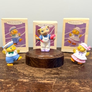 May include: A white ceramic mug with a black handle and the text "But First, Coffee" in a bold, black font. The mug is set against a blurred background, suggesting a cozy setting. The mug appears to be approximately 4 inches tall.