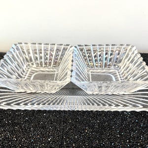 May include: A clear glass serving dish with two divided sections. The dish has a decorative, ribbed pattern.