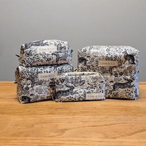 May include: A collection of five matching toiletry bags in varying sizes. The bags are white with a black rabbit and floral pattern. Each bag has a small tag that reads "Crow & Co."