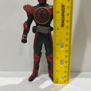 May include: A red and black action figure of a superhero with a red helmet and a black and gold belt. The figure is standing on a yellow ruler that measures 30 inches.