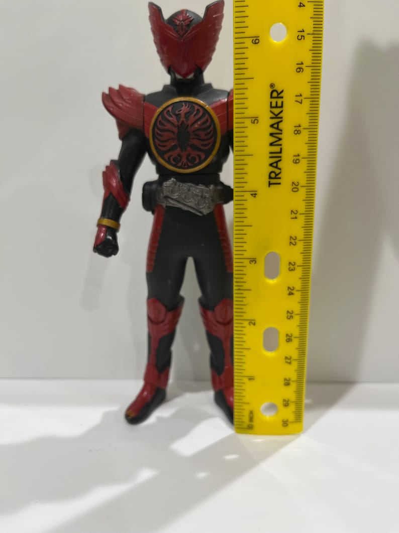 May include: A red and black action figure of a superhero with a red helmet and a black and gold belt. The figure is standing on a yellow ruler that measures 30 inches.