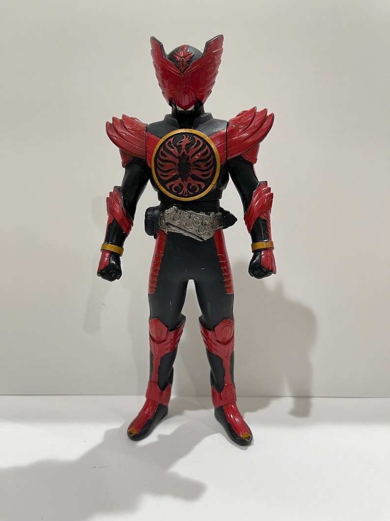 May include: A red and black action figure of a superhero with a bird-like helmet and a circular emblem on its chest.