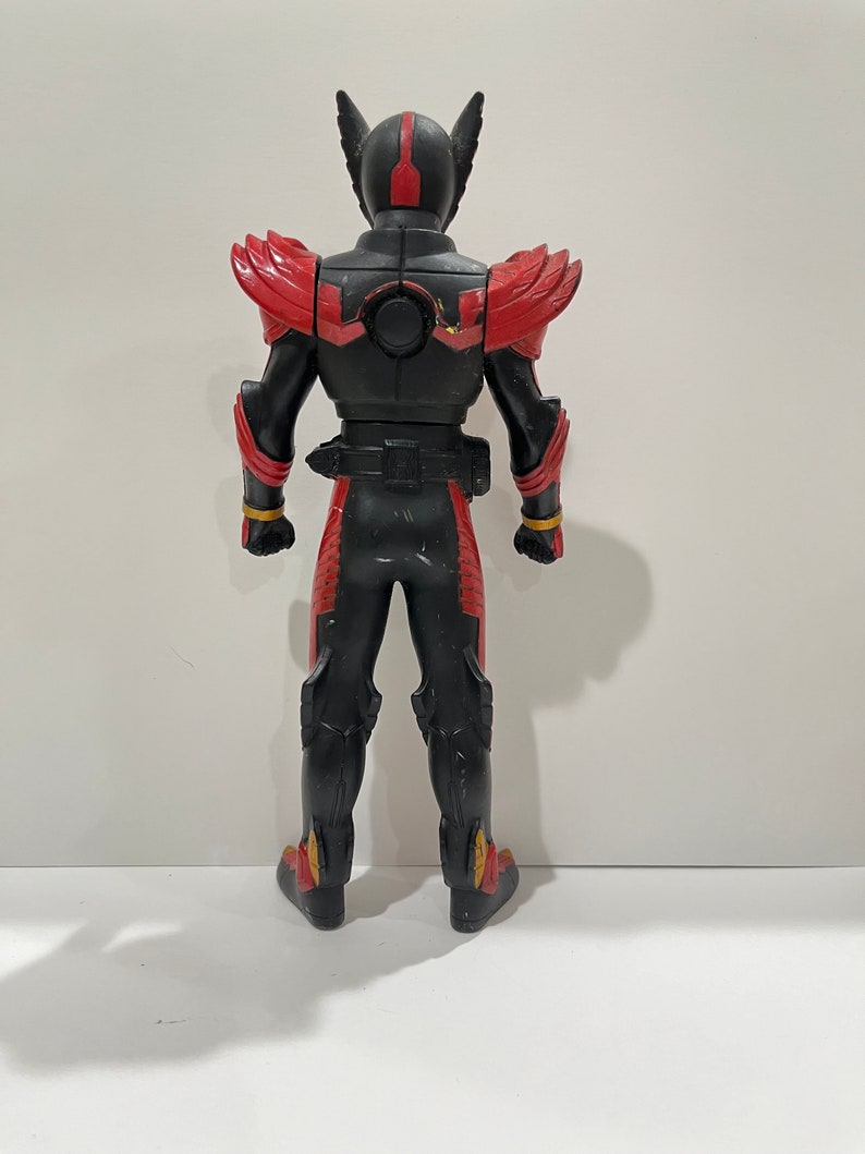 May include: Black and red action figure with a black helmet and gold accents. The figure is standing with its back to the camera.