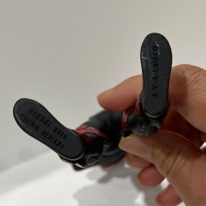 May include: Black and red action figure with the text "BANDAI 2010 CHINA 21216420" on one foot and "2010 1-T-A-T" on the other foot.