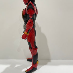 May include: A red and black action figure with a helmet and wings. The figure is standing on a white surface.