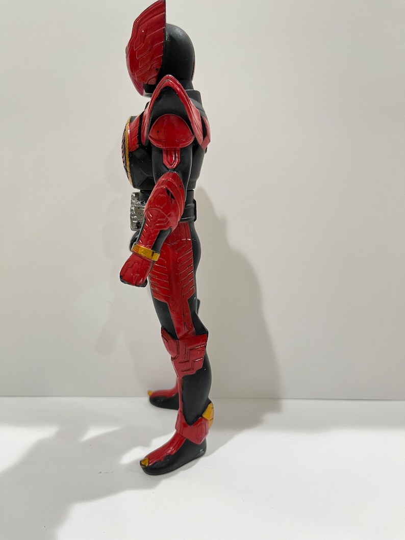 May include: A red and black action figure with a helmet and wings. The figure is standing on a white surface.