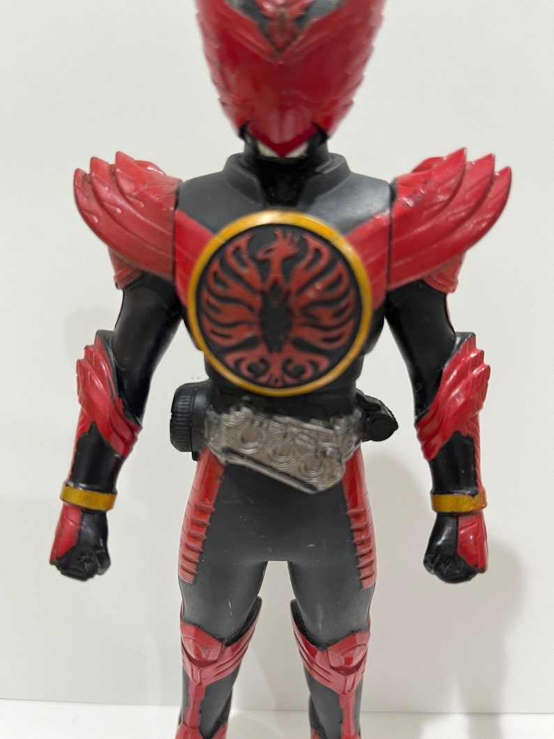 May include: A red and black action figure of a superhero with a red helmet and a black and gold belt. The figure has a red and gold symbol on its chest.