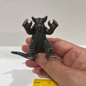 May include: A black and gray plastic toy monster with a spiky back and claws. The monster is about 2 inches tall.