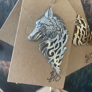 May include: Silver wolf head pendant with intricate filigree design. The pendant is on a brown paper tag with a price tag of $10.