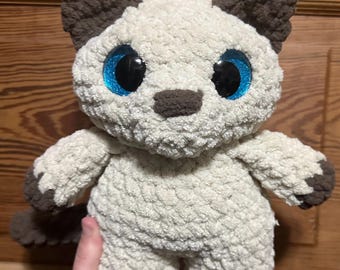 May include: A crocheted plush toy cat with brown ears and a white body. The cat has large blue eyes and a brown nose.