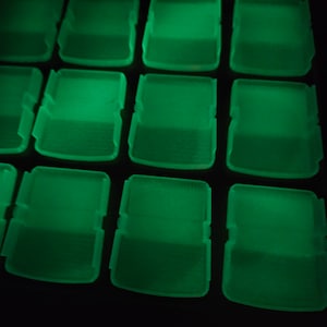 May include: A close-up of a set of 12 green plastic containers with lids. The containers are arranged in a grid pattern and are glowing in the dark.