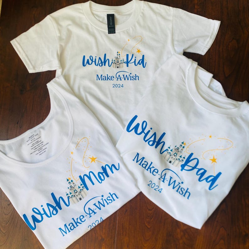 Pode incluir: Tr&ecirc;s camisetas brancas e uma regata com texto azul. As camisetas dizem "Wish Kid", "Wish Mom" e "Wish Dad", com "Make-A-Wish 2024" abaixo. Cada uma tem um castelo e estrelas cadentes.