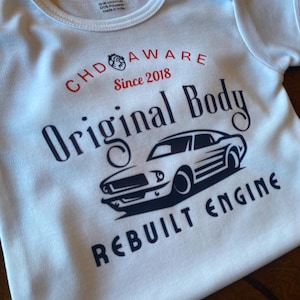 May include: White baby onesie with a black and white illustration of a classic car. The text "CHD AWARE Since 2018 Original Body REBUILT ENGINE" is printed on the onesie.