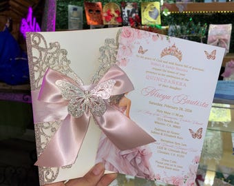 May include: A quinceañera invitation featuring a pink satin bow with a silver glitter butterfly accent. The invitation has a cream-colored background with a floral design and text that reads "Mireya Bautista".
