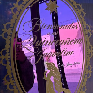 May include: A decorative mirror with gold filigree and the text "Bienvenidos a mi Quinceañera Jaqueline 13 de Junio, 2026". The mirror has a purple background and a silhouette of a woman.