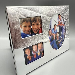 May include: Silver multi-photo frame with a textured surface. The frame has three openings for photos, one oval and two rectangular. The frame is standing on a white surface.