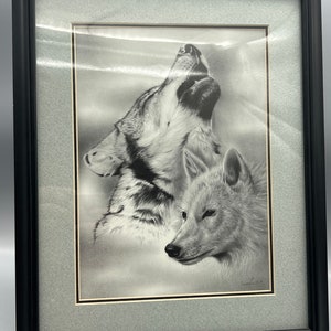 May include: A black and white framed print of two wolves howling at the moon. The wolves are drawn in a realistic style and the print is signed by the artist.