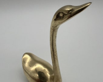 Può includere: Una statuetta di cigno in ottone dorato con un collo lungo e un corpo curvo.