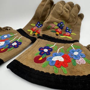 May include: A pair of brown leather gloves with beaded floral designs in shades of blue, red, green, and white. The gloves have black trim and fringe.