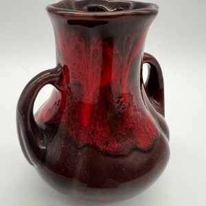 May include: A small, brown ceramic vase with two handles. The vase has a red glaze with a marbled effect.