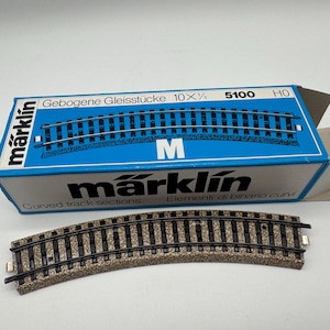 May include: Curved model train track sections with a blue and white box. The box reads "Gebogene Gleisstücke 10 x 1/2" and "Marklin". The track is brown and black.