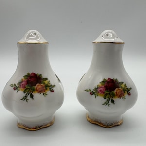 以下が含まれることがあります： 金色の縁取りと赤、黄、緑のバラの花柄が施された白い磁器製の塩と胡椒入れのセットです。