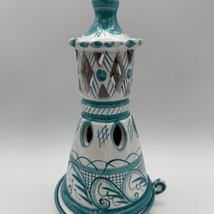 Puede incluir: Un quemador de incienso de cerámica blanca con un diseño geométrico azul y blanco. El quemador tiene una base cónica alta y una parte superior decorativa con un remate puntiagudo.