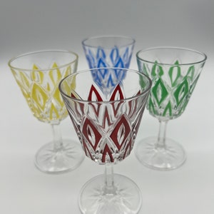 Puede incluir: Juego de cuatro vasos de chupito de vidrio transparente con un patrón geométrico. Cada vaso tiene un diseño de color diferente: amarillo, azul, verde y rojo.