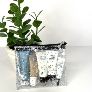 May include: A clear plastic zippered pouch with a star pattern and five small bottles of skincare products inside. The bottles are labeled "Summer Fridays", "La Mer", "La Prairie", "Chanel", and "Bio-Oil".