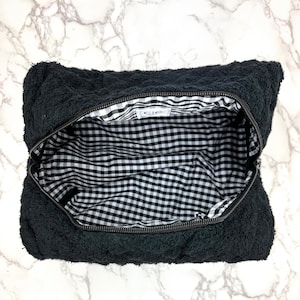 May include: Black zippered pouch with a black and white checkered lining. The pouch is made of a soft, textured fabric.