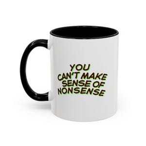 Puede incluir: Taza de cerámica blanca con asa e interior negros. La taza presenta el texto "YOU CAN'T MAKE SENSE OF NONSENSE" en letras marrones con contorno verde.