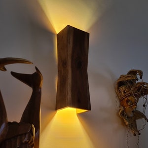 Könnte beinhalten: Eine Wandleuchte aus Holz mit einem warmen Licht, das durch die Öffnung scheint. Die Leuchte ist aus dunklem Holz mit einer natürlichen Maserung.